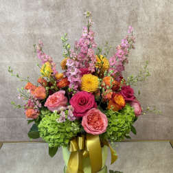 Colorful bouquet of pink, orange, and yellow flowers in a green box with a gold ribbon