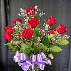 Red roses in a glass vase with a purple ribbon