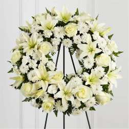 White floral wreath on a black stand with roses and lilies