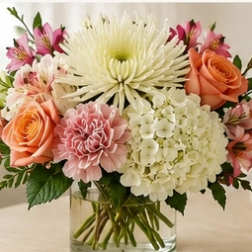 Mixed bouquet of pink and peach flowers in a clear glass vase