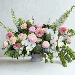 Low floral arrangement with pink blooms, white orchids, and green accents in a gray vase