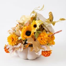 Orange and yellow floral arrangement in a white pumpkin container