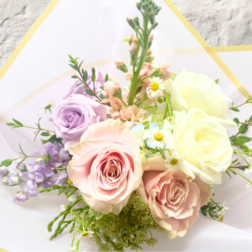 Bouquet of pastel roses and small daisies wrapped in white paper