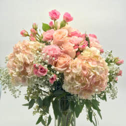 Tall glass vase arrangement of blush hydrangeas, pink roses, carnations, and baby's breath.