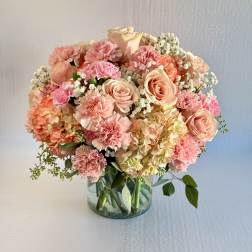 Round arrangement of peach roses, pink carnations and hydrangeas in a clear glass vase