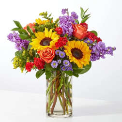 Bouquet of sunflowers, roses, carnations, and purple flowers in a glass vase
