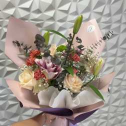 Handheld bouquet of roses, lilies, and carnations wrapped in pink and purple paper