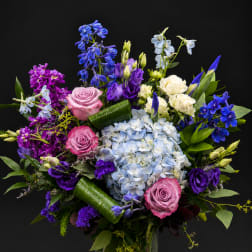 Mixed bouquet of roses, hydrangea, and purple blooms in a glass vase