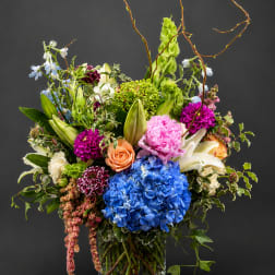 Colorful mixed flower arrangement in a clear glass vase with tall curly branches