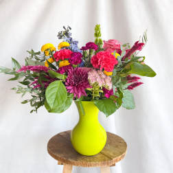 Mixed bouquet in a bright yellow vase with pink, purple, and yellow flowers