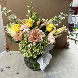 Mixed bouquet in a glass vase with yellow roses, lilies, and pale pink blooms