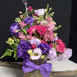 Colorful bouquet of pink and purple flowers in a textured glass vase with a purple ribbon