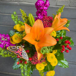 Bouquet of orange lilies, yellow mums, and purple flowers with a butterfly accent