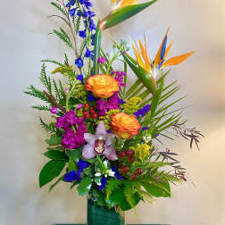 Tropical bouquet with orange bird-of-paradise and mixed blooms in a glass vase