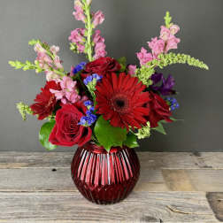 Red roses and gerbera daisies in a ribbed red glass vase