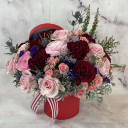 Pink and burgundy rose arrangement in a red hat box with a striped ribbon