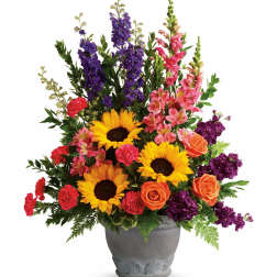 Mixed bouquet with sunflowers, roses, carnations, and purple spikes in a gray vase
