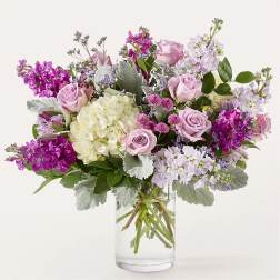 Bouquet of pink roses, hydrangea, and purple flowers in a clear glass vase