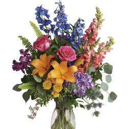 Colorful mixed bouquet in a clear glass vase with lilies, roses, and blue flowers