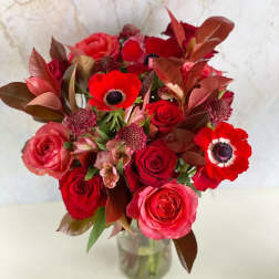 Red rose bouquet with red anemones in a glass vase