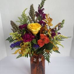 Mixed bouquet of roses and fall flowers in an amber glass vase