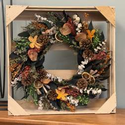 Rustic wreath with pinecones, dried orange slices, and orange flowers in a wooden frame