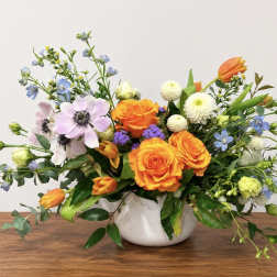 Mixed bouquet of orange roses, tulips, and pastel flowers in a white vase