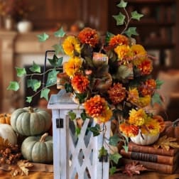 Orange and yellow flower arrangement in a white lantern-style holder