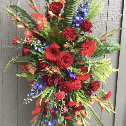 Tall standing floral spray with red roses, gerbera daisies, and blue accents