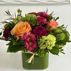 Mixed bouquet of orange and pink flowers in a green square vase