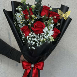 Bouquet of red roses with white filler flowers wrapped in black paper and a red ribbon