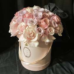 Pink and white roses arranged in a round hat box with a black polka-dot ribbon