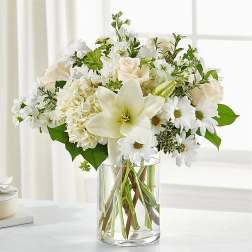 White roses, lilies, and daisies arranged in a clear glass vase