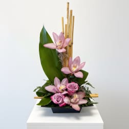 Pink orchids and roses arranged in a black container with bamboo accents