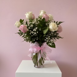 Pink and white roses in a glass vase with a pink ribbon