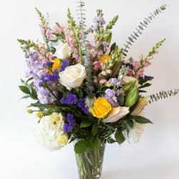 Mixed bouquet of roses, lilies, and purple flowers in a clear glass vase
