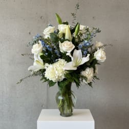 White roses and lilies arranged in a glass vase with blue accents.