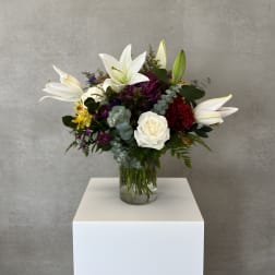 Mixed bouquet with white lilies, roses, and purple flowers in a glass vase