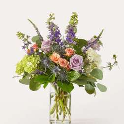 Mixed bouquet of roses, hydrangeas, and purple spikes in a clear glass vase