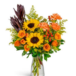 Bouquet of sunflowers, orange roses, and carnations in a clear glass vase