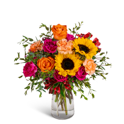 Bouquet of orange and pink flowers with sunflowers in a clear glass vase