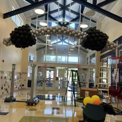 Black and gray balloon arch in a lobby with ladders and chairs