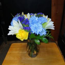 Mixed bouquet of blue, white, yellow, and purple flowers in a glass vase