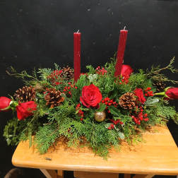 Red roses and candles in a low evergreen centerpiece with pinecones