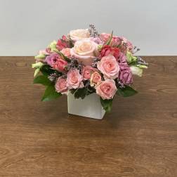 Pink and peach roses arranged in a white square vase