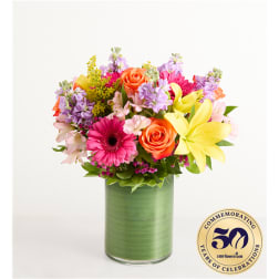 Colorful mixed bouquet in a green glass vase with roses, lilies, and daisies