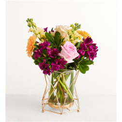 Mixed bouquet of pink, purple, and yellow flowers in a glass vase