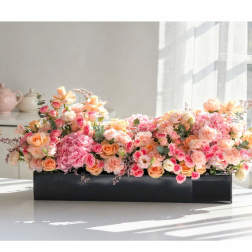 Low floral arrangement of pink and peach roses in a black rectangular container