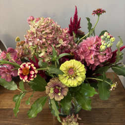 Mixed bouquet with pink hydrangeas, zinnias, and yellow blooms in a glass vase