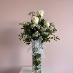 White roses and baby's breath in a tall glass vase with a white ribbon